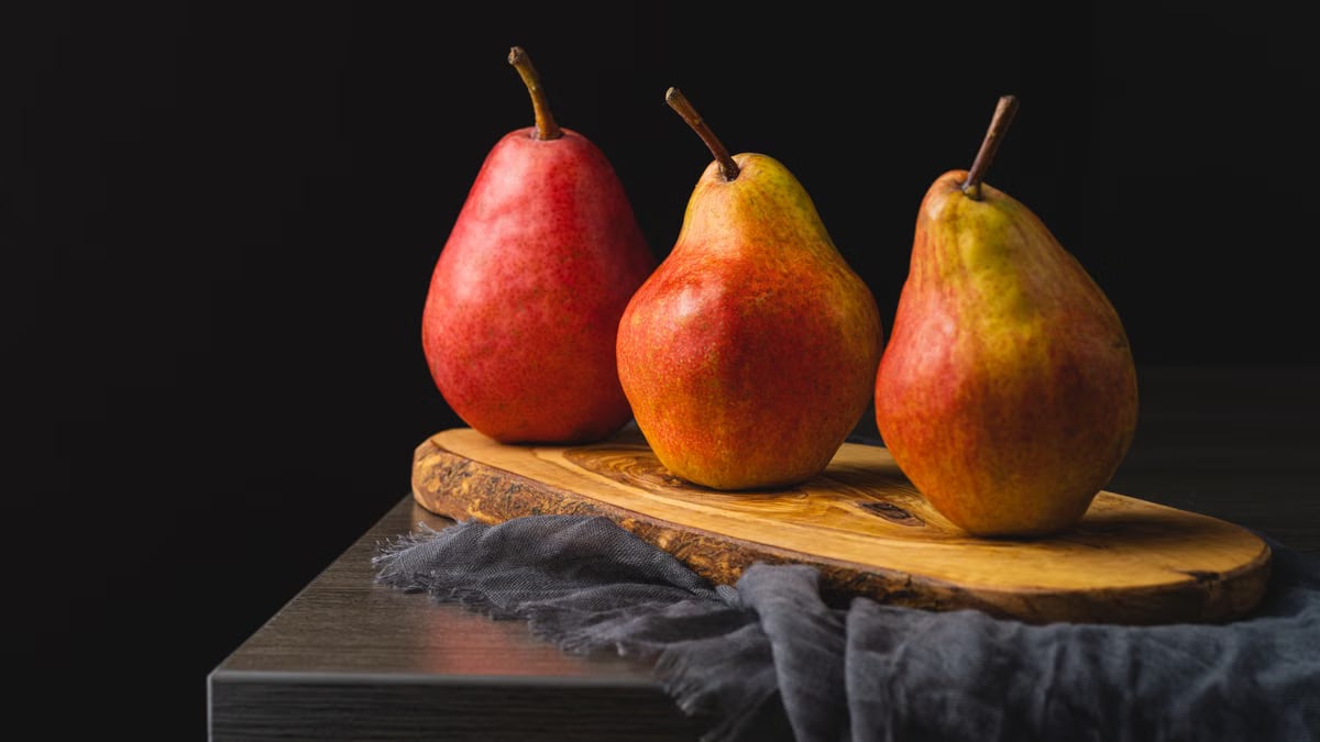 Beautiful display of three ripe red pears on a wooden cutting board.